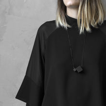 Load image into Gallery viewer, A woman with a blond hair wearing the Black MODULODUE Necklace with a black bluse on a grey background
