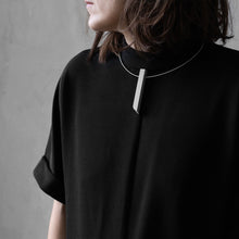 Load image into Gallery viewer, A woman with a blond hair wearing the Grey Column Necklace with a black bluse on a grey background