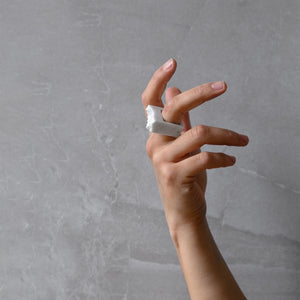 A woman wearing the Bianco Ring on their finger on grey background