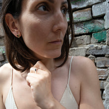 Laden Sie das Bild in den Galerie-Viewer, Mini square earrings worn in an urban setting with natural light and geometric shadows.
