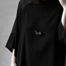 Load image into Gallery viewer, A woman with a blond hair wearing the Black MODULOTRE Necklace with a black bluse on a grey background 