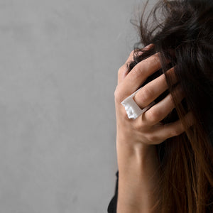 A woman wearing the Bianco Ring on their finger while touching her hair on grey background