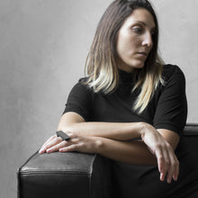 Load image into Gallery viewer, A woman wearing the Asteroid Ring on their ring finger while sitting on a black leather sofa with a concrete grey background