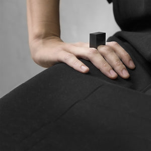 A woman wearing the Megalith Ring on their ring finger while sitting on a black on a concrete grey background