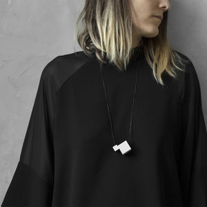 A woman with a blond hair wearing the Grey MODULODUE Necklace with a black bluse on a grey background 