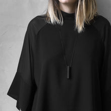 Load image into Gallery viewer, A woman with a blond hair wearing the Black MODULOQUATTRO Necklace with a black bluse on a grey background 