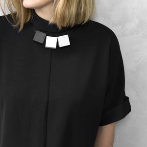 A woman with a blond hair wearing the Zero Elements Necklace with a black bluse on a grey background 
