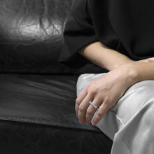 Load image into Gallery viewer, A person wearing the Aluminium Square Ring on their ring finger while sitting on a black leather sofa