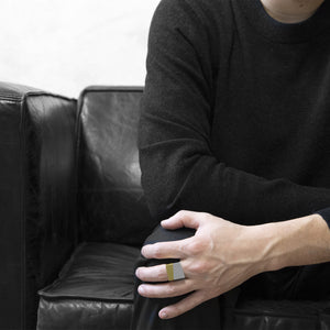 man wearing the Assembled ring, a combination of Aluminium square ring and brass square ring, seat on black sofa